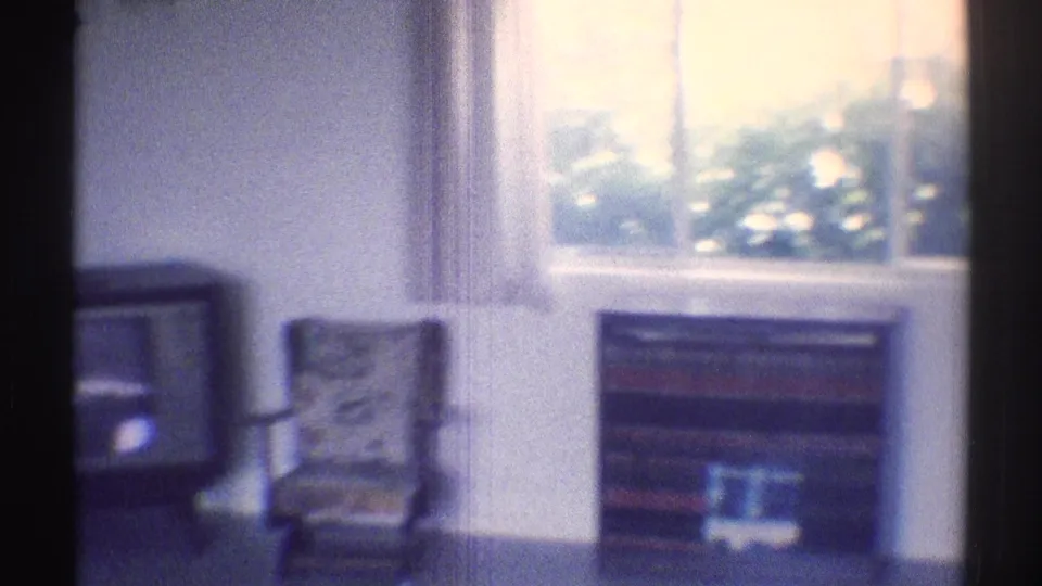 1969 Woodland Hills home-movie interior showing a small television, patterned chair, bright window, and bookshelf in a bedroom or sitting area.