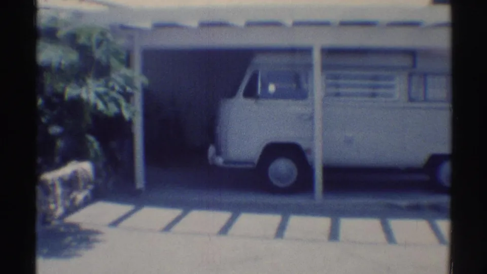 Side view of a white Volkswagen Type 2-style van parked beneath a residential carport in Woodland Hills, 1969.