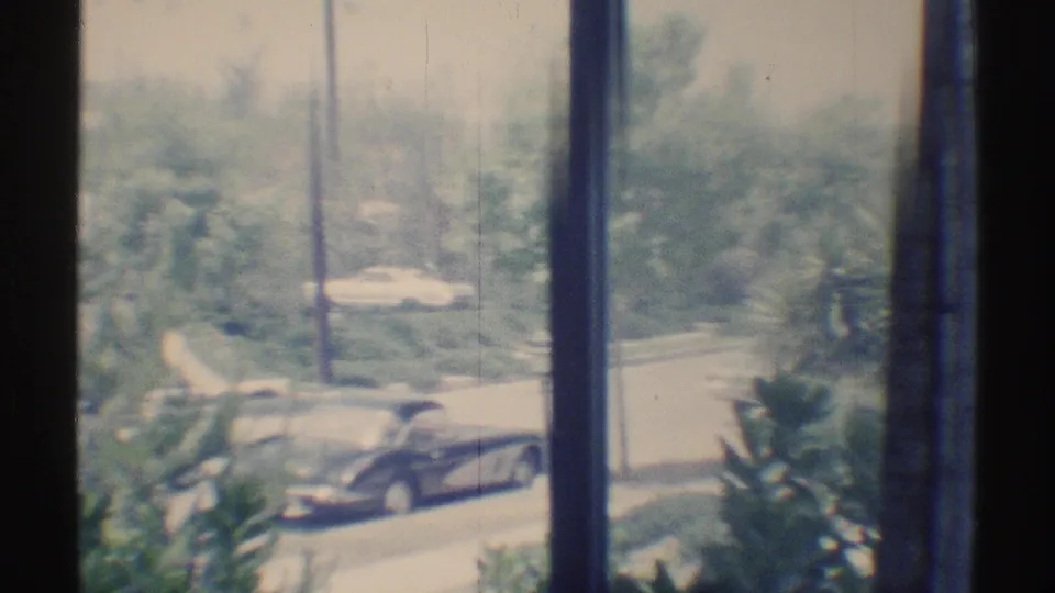 1969 Woodland Hills home-movie view through an interior window toward parked cars and trees along a suburban street.