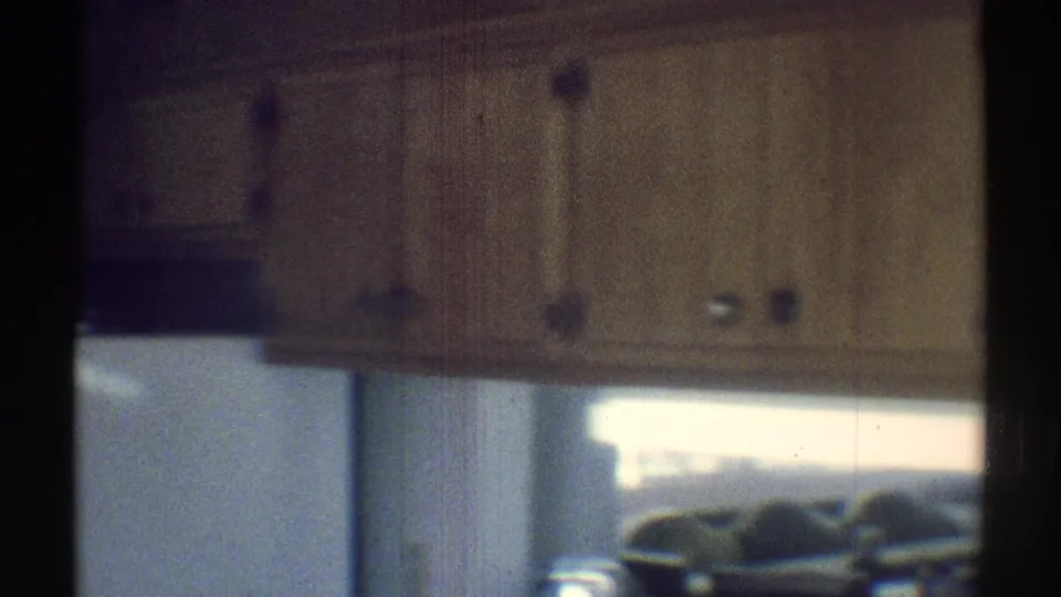 1969 kitchen detail with wood cabinet doors, countertop area, vertical blinds, and soft daylight in a private Woodland Hills interior.