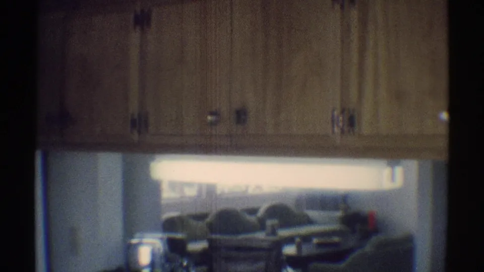 1969 Woodland Hills home-movie frame showing wood kitchen cabinetry and a counter, with a living room and couches in the background.