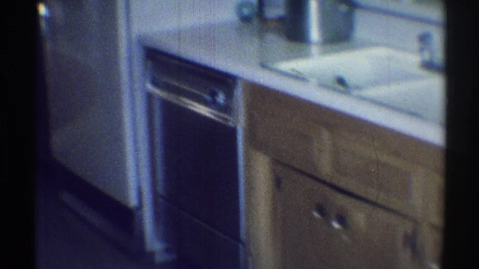 1969 Woodland Hills kitchen frame showing a built-in oven, sink area, white counter, and wood cabinetry.