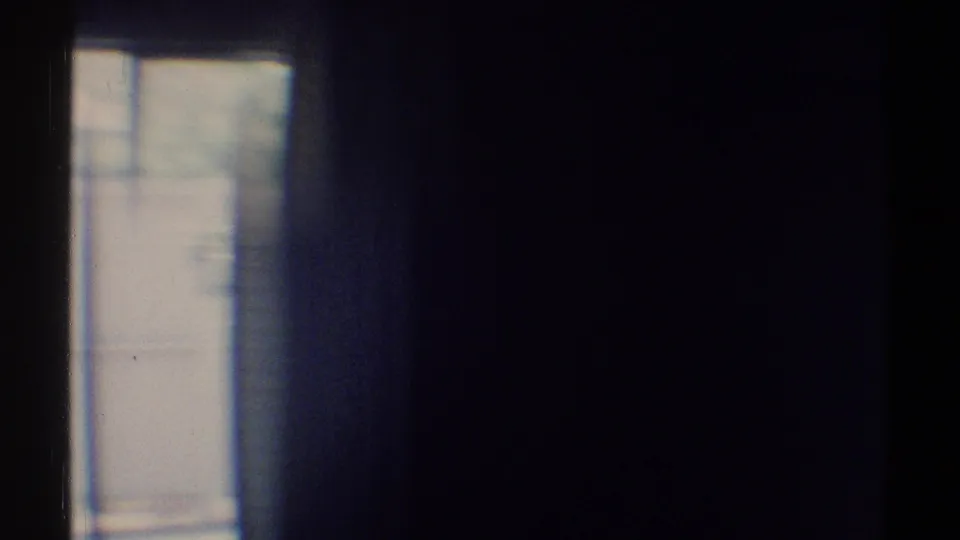 Blue-tinted 1969 home-movie frame showing a darkened interior edge, bright window, and surrounding wall surfaces.