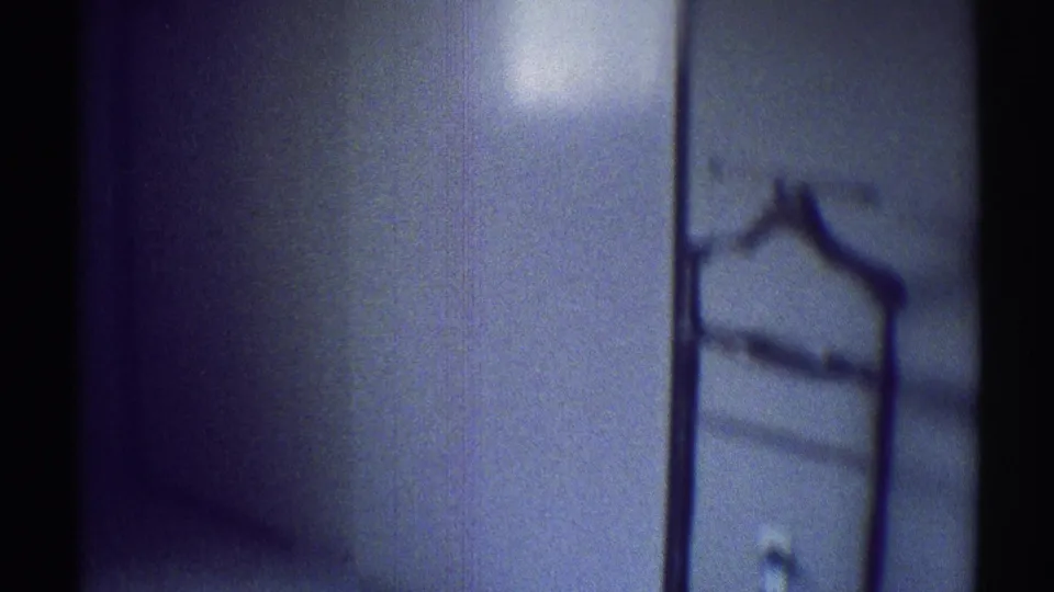 1969 Woodland Hills interior frame showing a pale wall and a wall-mounted coat rack or towel rack in soft blue-tinted light.