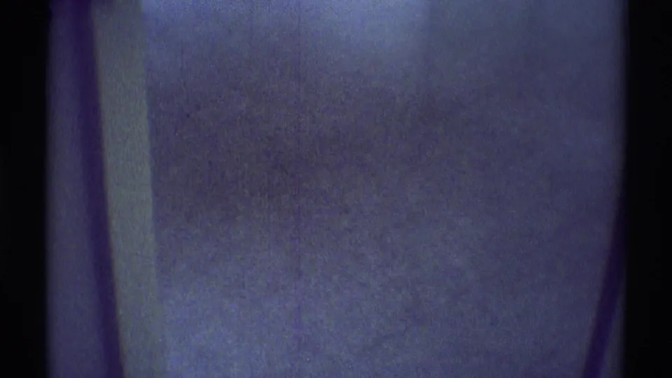 Dark 1969 Woodland Hills interior frame with a vertical wall or doorway edge, blue-tinted shadows, and heavy film grain.