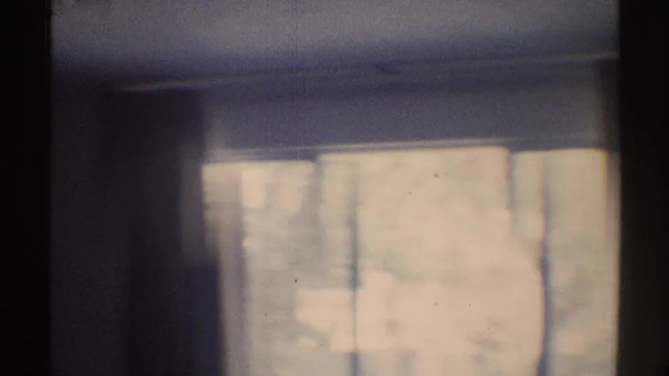 1969 Woodland Hills home-movie frame showing a dark room and a window with pale curtains, softened by grain and low-light exposure.