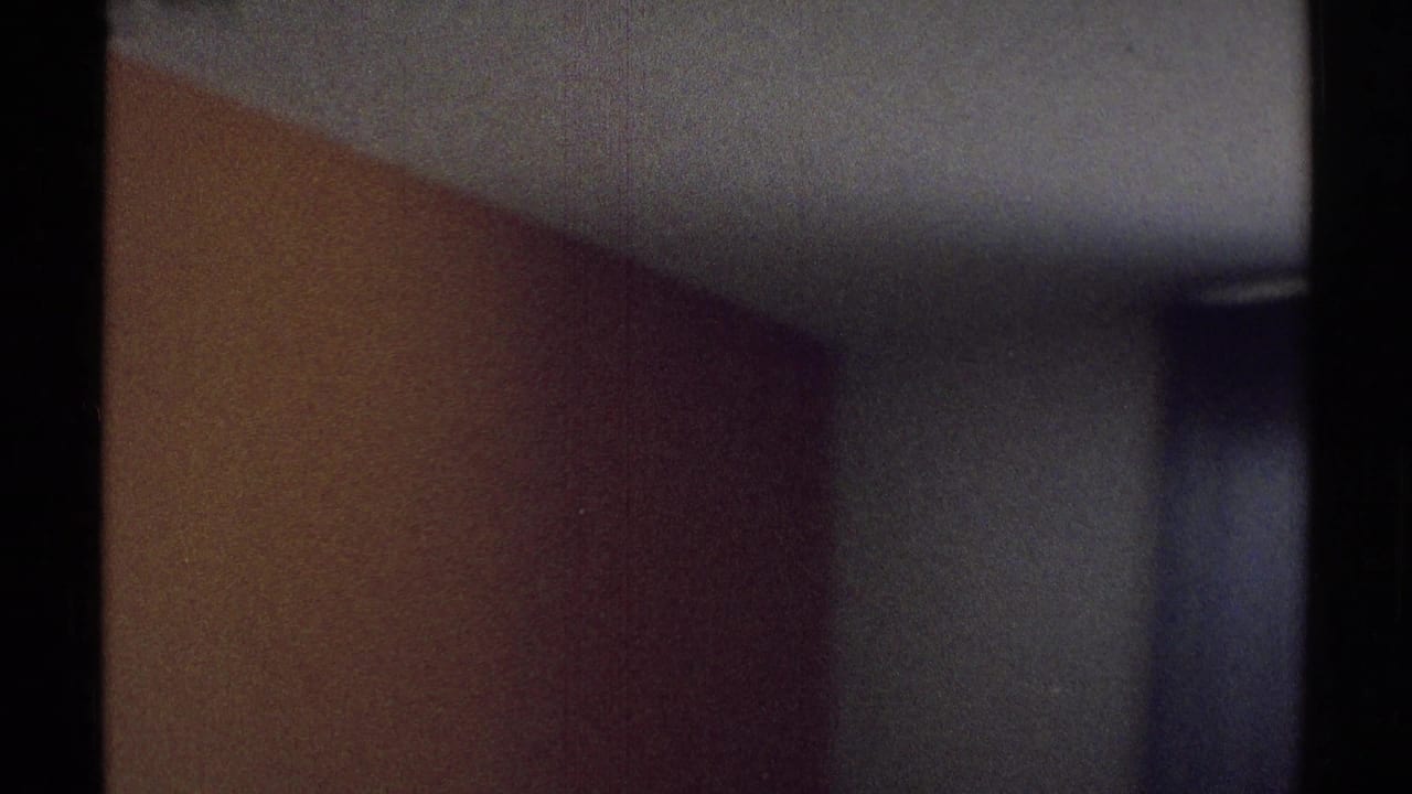 Dim bedroom wall and doorway with dark vertical film edge.