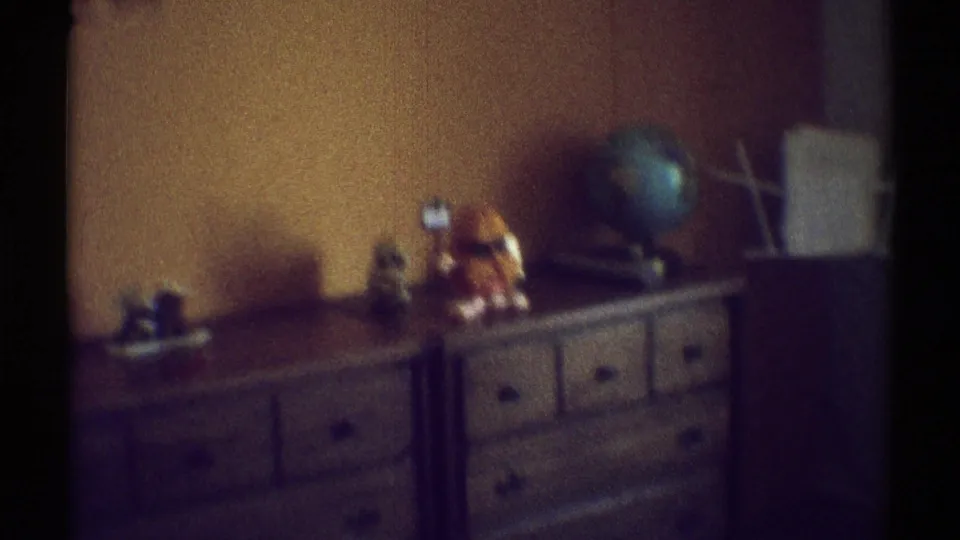 Brown wooden dressers sit against an orange bedroom wall with a globe, small objects, and a plush toy on top.