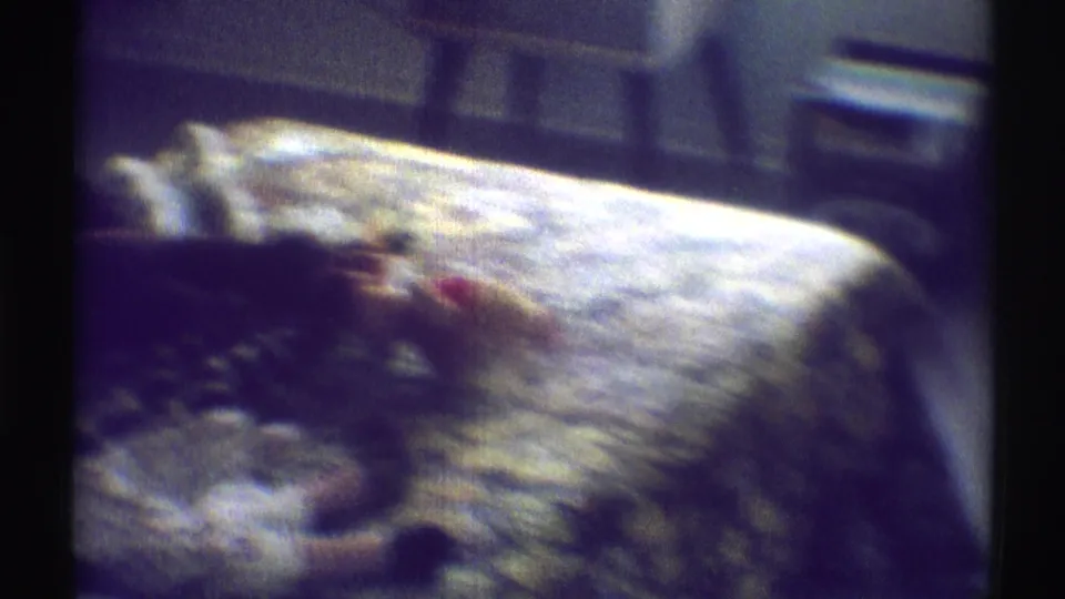 A softly focused 1969 bedroom view shows a bed with a patterned spread and shadowed furniture nearby.