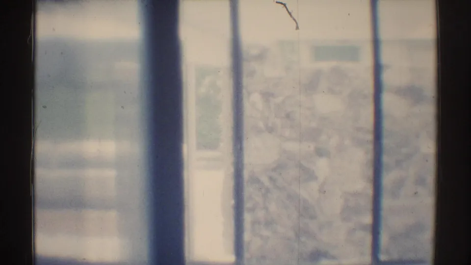 1969 Woodland Hills home-movie frame looking through vertical window bars toward a bright, blurred exterior scene.