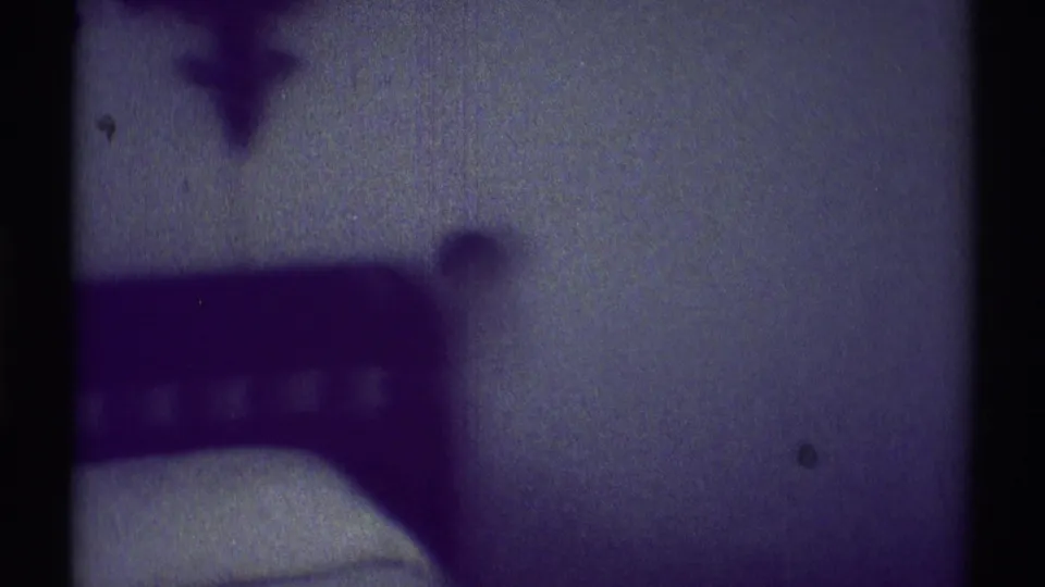 A low-lit bedroom corner shows the edge of a bed and a dark furniture form in the 1969 Woodland Hills footage.