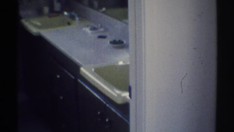 Woodland Hills home bathroom with a long counter, two sinks, dark cabinetry, and a mirror area, seen in warm 1969 8mm footage.