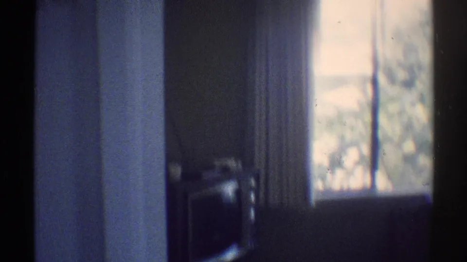 1969 Woodland Hills interior frame with a bright curtained window, blue-toned wall, doorway edge, and dark furniture shape.
