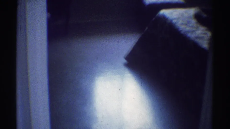 1969 Woodland Hills home interior showing a bed beneath window light, doorway framing, floor reflection, and soft blue film cast.