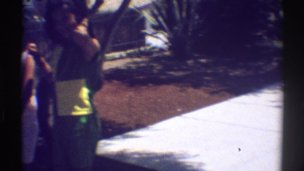 In 1969 Woodland Hills home-movie footage, two adults appear to talk near a bright concrete patio framed by garden plants.