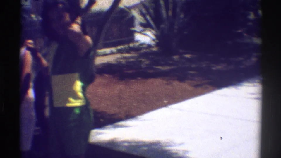 In 1969 Woodland Hills home-movie footage, two adults appear to talk near a bright concrete patio framed by garden plants.