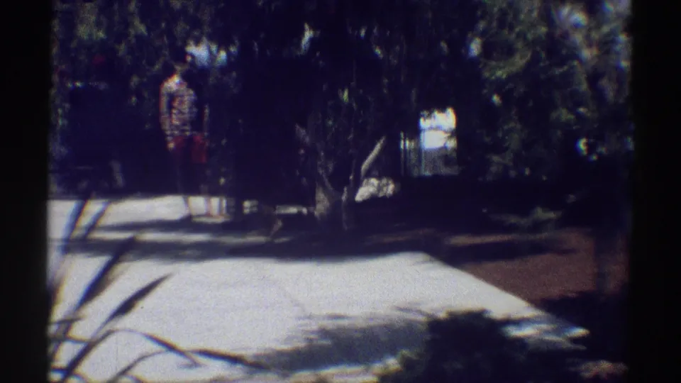 A shaded Woodland Hills residential path or driveway with trees and a distant person near the background, captured on 8mm film in 1969.