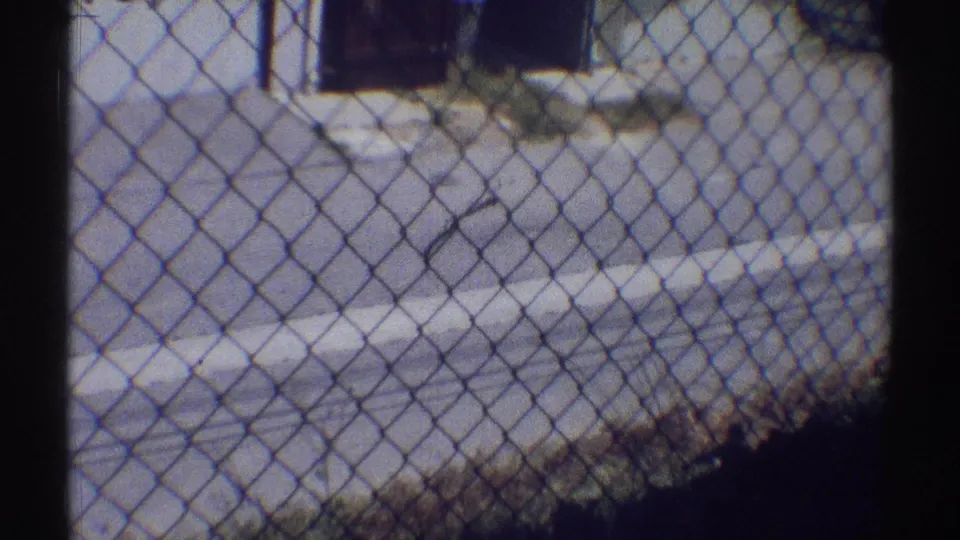 Chain-link fencing crosses the foreground of a sunlit Woodland Hills residential driveway or walkway in this 1969 home-movie frame.