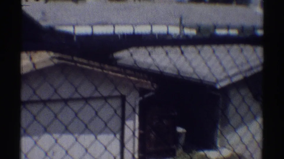 A chain-link fence frames a low covered structure, possibly a carport or shed, beside a bright paved area in Woodland Hills in 1969.