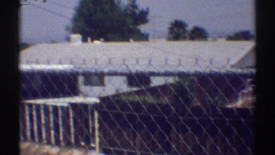 1969 Woodland Hills suburban house roof and yard details seen through chain-link fencing.