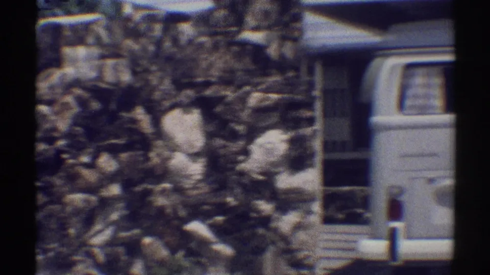 1969 Woodland Hills frame with textured stonework and the rear of a light-colored van parked beside a house.