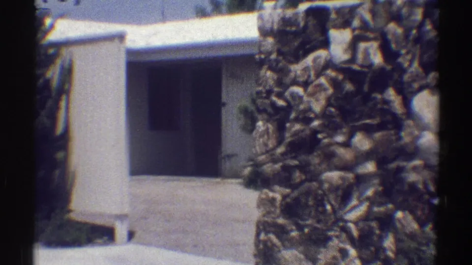 Woodland Hills 1969 frame showing a white residential entrance, paved walkway, and rough stone wall in close foreground.
