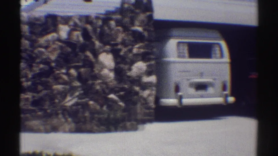 1969 Woodland Hills home-movie frame showing a stone wall, driveway, and white van parked near a residential garage.