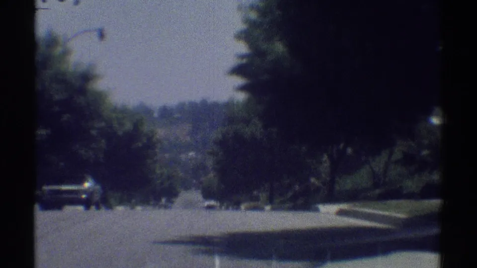 1969 Woodland Hills home-movie frame looking down a tree-lined residential street with cars in the distance.
