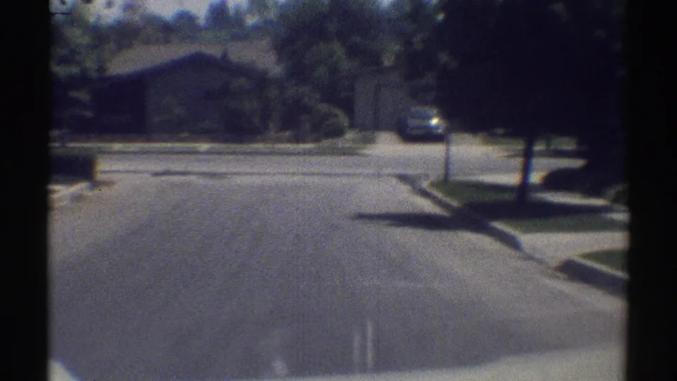 1969 Woodland Hills suburban street scene with a driveway, parked car, trees, and low homes seen through the windshield area.