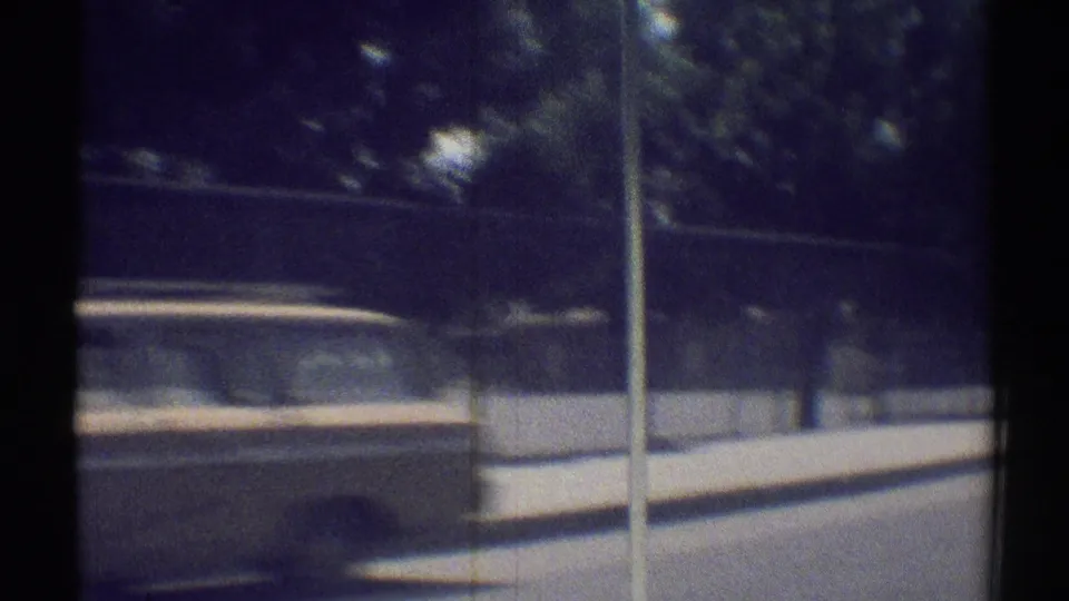 A late-1960s Woodland Hills street view shows a station wagon near a curb, fence, trees, and sidewalk in soft 8mm motion.