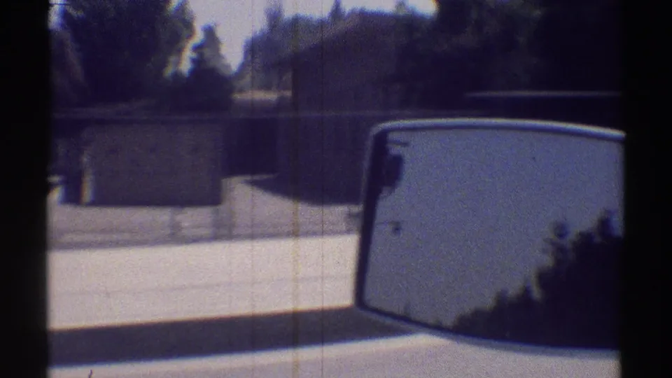 Woodland Hills road view from inside a car, with side mirror, curb, trees, and fencing visible in 1969 home-movie footage.