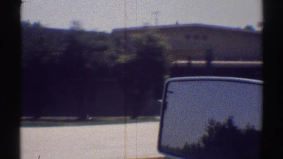 Suburban Woodland Hills street scene from a moving vehicle, with a low building, trees, curb, and side mirror visible.