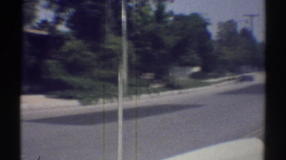 A late-1960s Woodland Hills driving POV shows a curving street bordered by trees, curb lines, and a utility pole.
