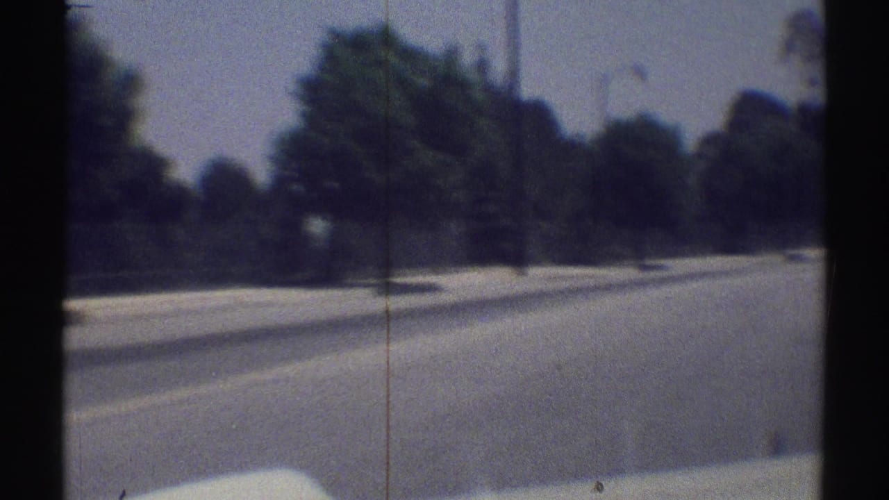 1969 Woodland Hills home-movie frame showing a fast moving view along a broad road with trees, streetlights, and soft 8mm blur.