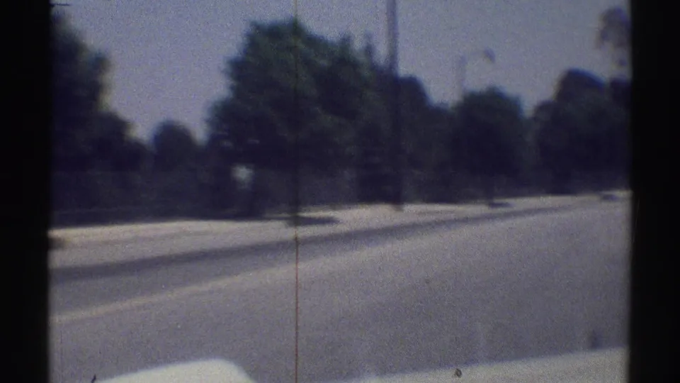1969 Woodland Hills home-movie frame showing a fast moving view along a broad road with trees, streetlights, and soft 8mm blur.