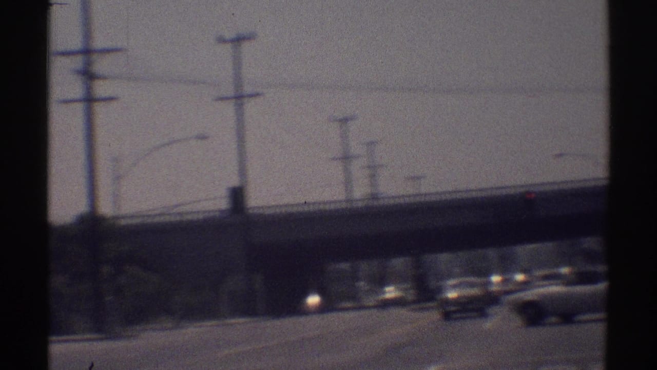 1969 Woodland Hills road footage shows the camera nearing an overpass as period cars move through sun glare.
