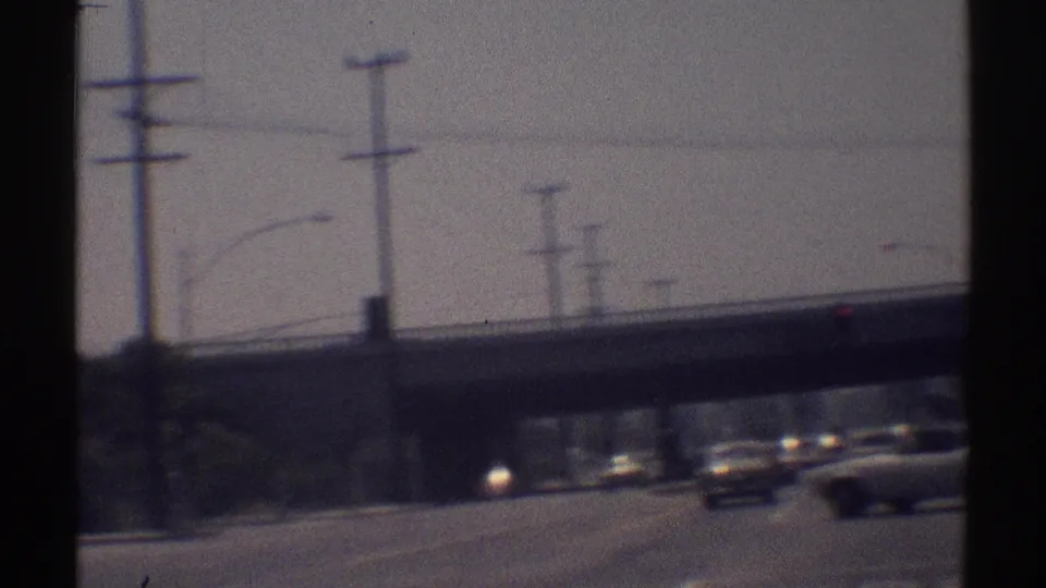 1969 Woodland Hills road footage shows the camera nearing an overpass as period cars move through sun glare.