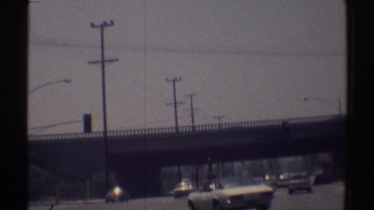 Late-frame 8mm view of 1969 Woodland Hills traffic passing beneath a concrete overpass with utility poles overhead.