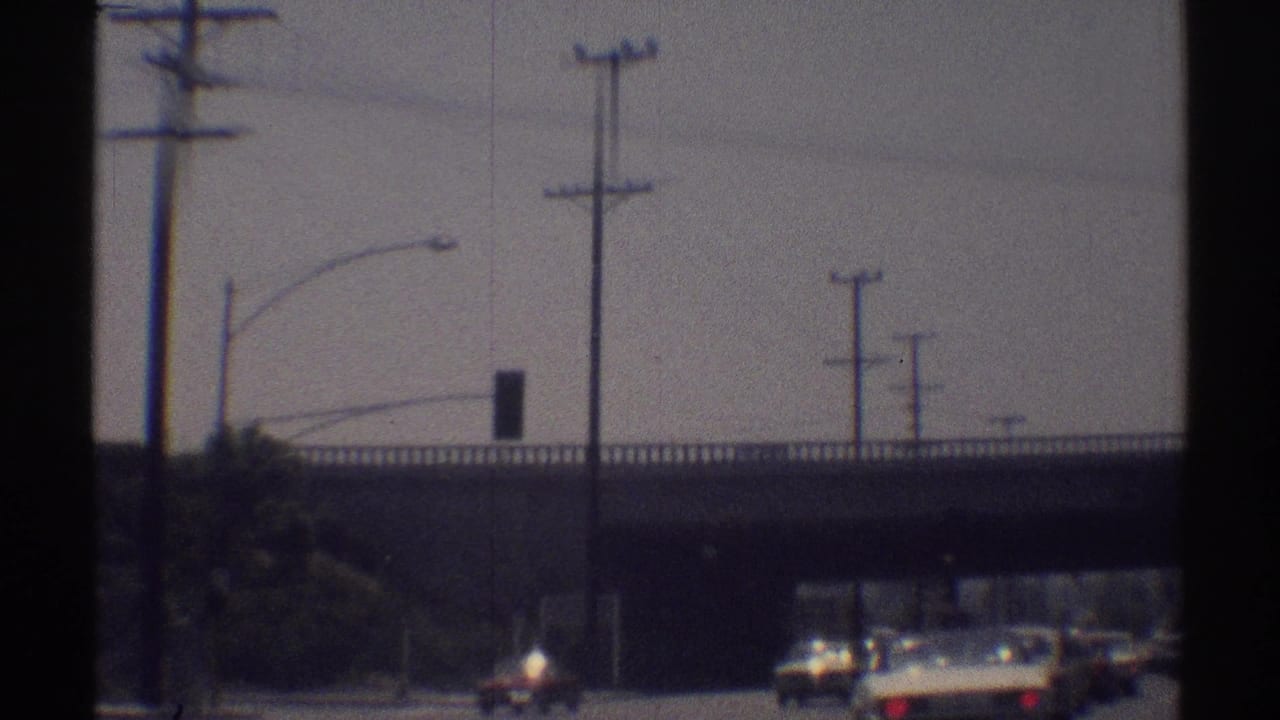 Cars approach an overpass on a sunlit multi-lane road with utility poles nearby.