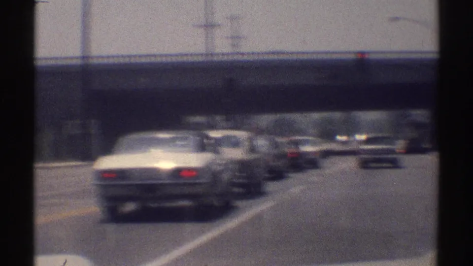 1969 Woodland Hills traffic seen from a moving vehicle, with several cars, lane stripes, and an overpass ahead.