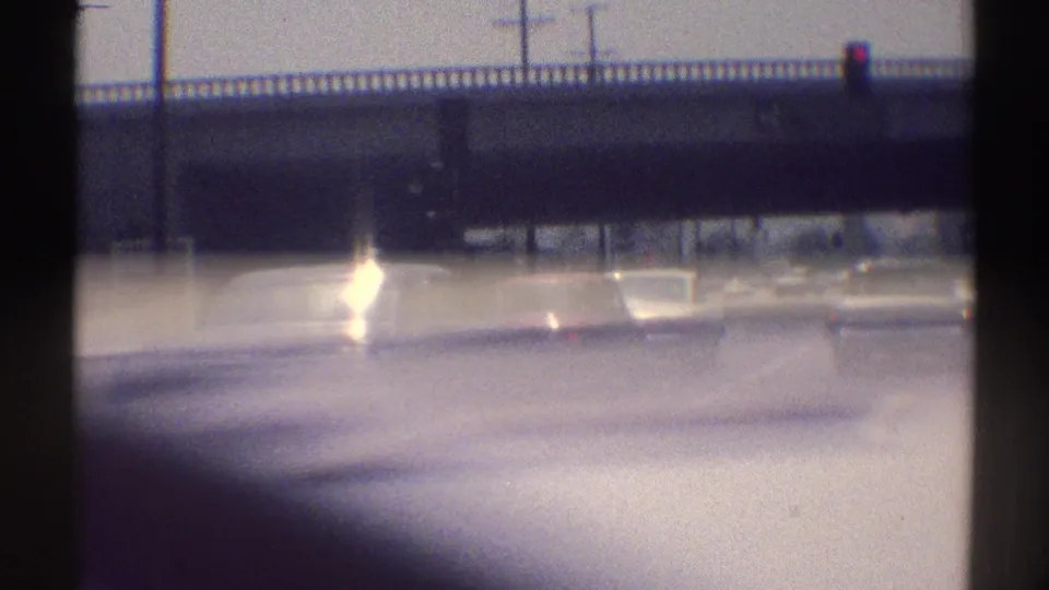 Sun-glared 1969 Woodland Hills roadway view with an overpass, traffic signals, and vehicles ahead.