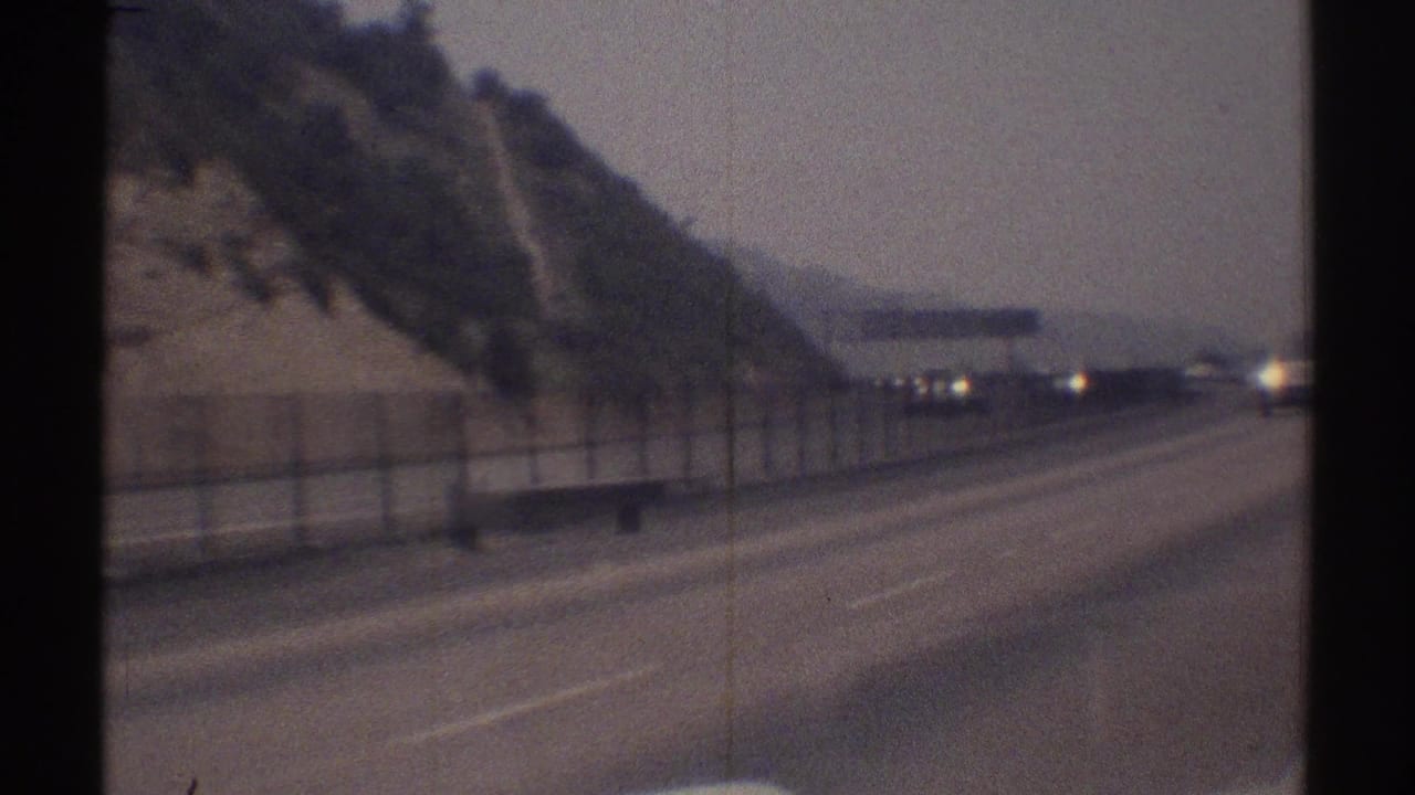 Wide highway view through a moving vehicle windshield with hillside and distant traffic.