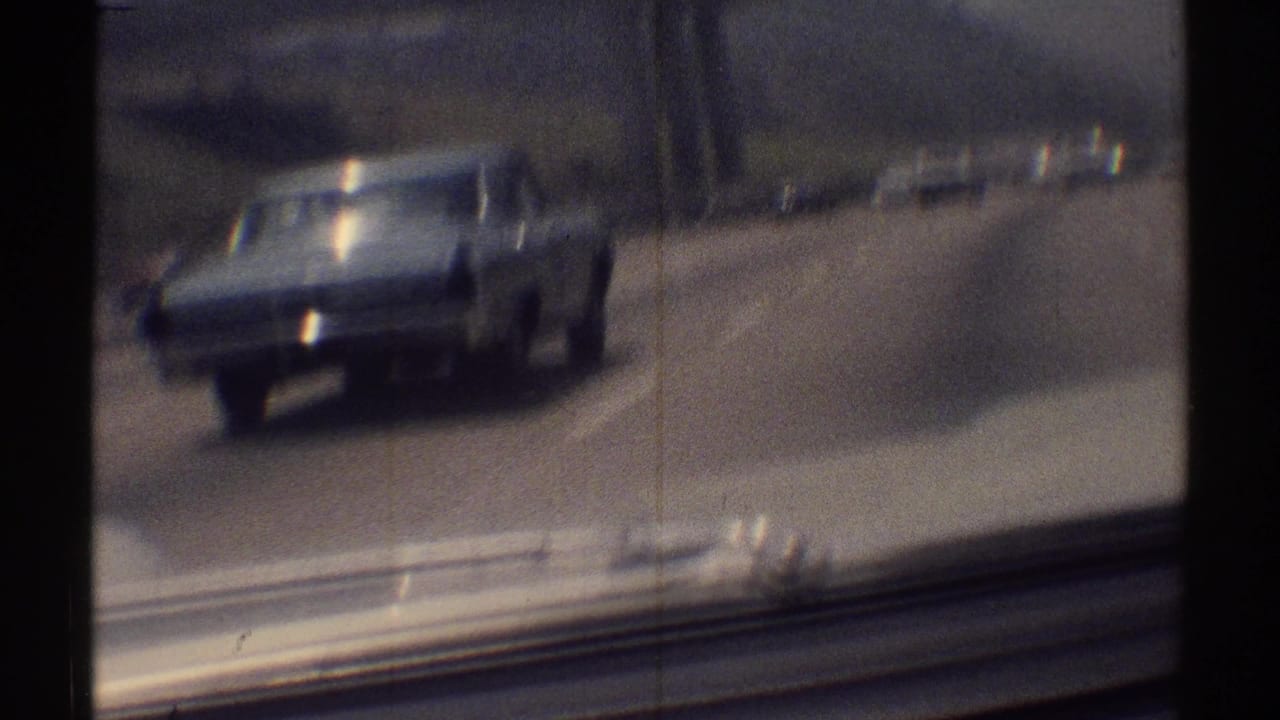 Light-colored classic sedan seen ahead on a highway through a vehicle windshield.