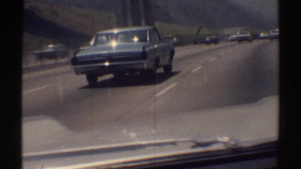Rear view of a light-colored classic sedan on a 1969 Woodland Hills highway, with other traffic visible farther ahead.