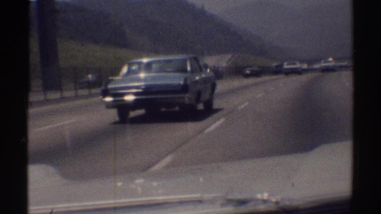 1969 Woodland Hills highway view from a moving car, with a blue sedan approaching beside distant traffic and low hills.