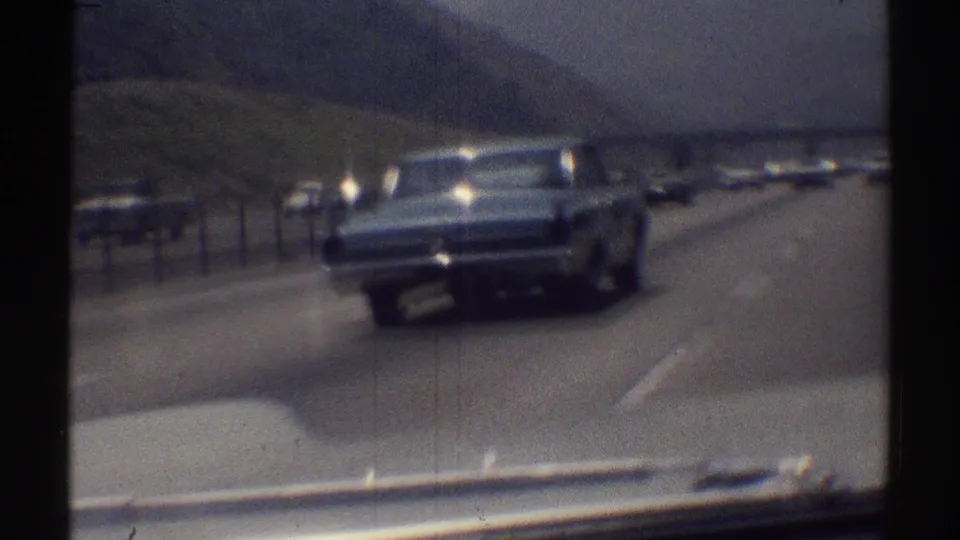 Passenger-shot 8mm frame of a classic sedan nearing the camera on a California highway in 1969.
