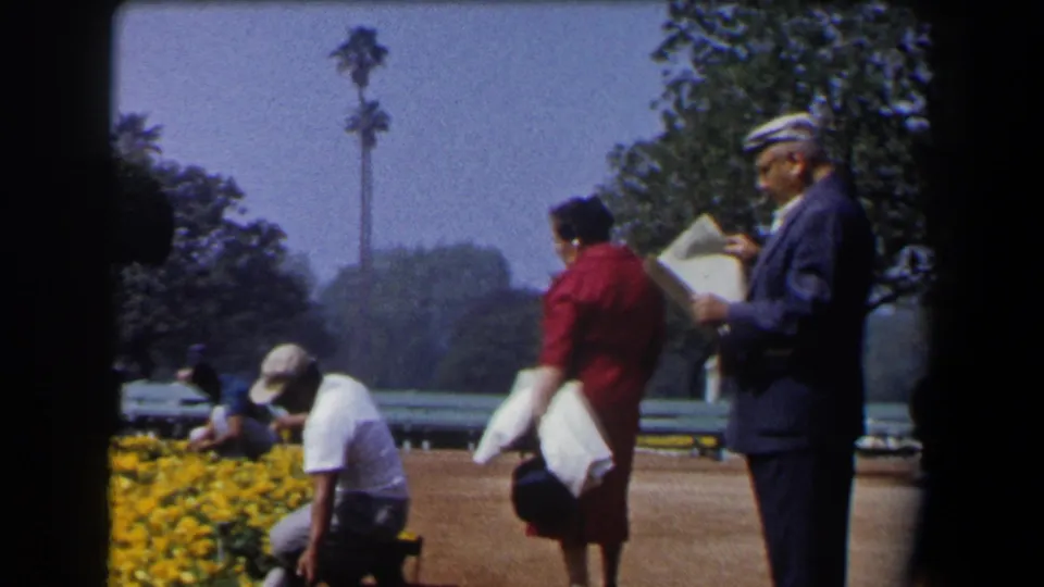 California 1958 garden frame with a suited man holding a newspaper, a woman in red, and a gardener kneeling by yellow flower beds.