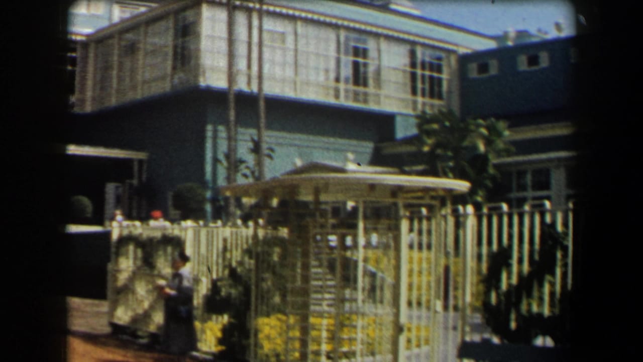 1958 California home-movie view of the blue house and garden entrance, with people visible near the fence.