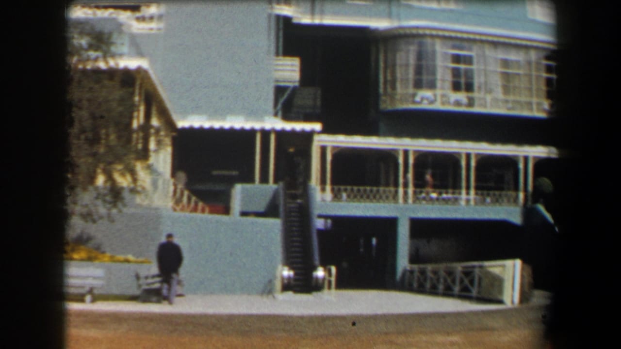 Man in dark clothing walking near a pale blue building with awnings and stairs.