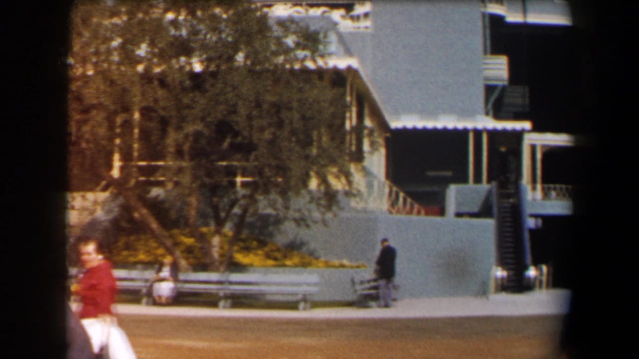 Woman in red walking across a sunny frontage with benches and a tree.